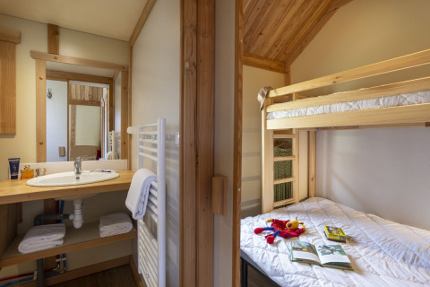 Interior del Montana Chalet en Huttopia Bourg Saint-Maurice con litera, juguetes en la cama y baño visible.