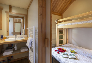 Interior del Montana Chalet en Huttopia Bourg Saint-Maurice con litera, juguetes en la cama y baño visible.