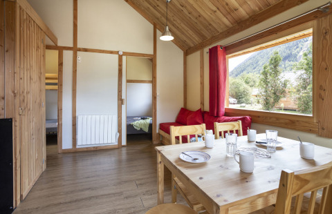 Vista interior del Montana Chalet en Huttopia Bourg Saint-Maurice con muebles de madera y ventana panorámica.