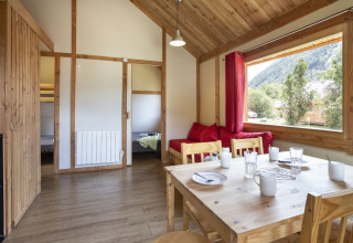 Vista interior del Montana Chalet en Huttopia Bourg Saint-Maurice con muebles de madera y ventana panorámica.