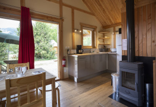 Interior del chalé Montana en Huttopia Bourg Saint-Maurice, Francia, con cocina moderna y estufa de leña.
