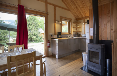 Interior of Montana Chalet at Huttopia Bourg Saint-Maurice, France, showing kitchen, dining area, and wood stove.
