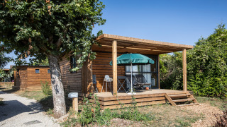 Træhytte Chalet Evasion med terrasse, havebord og parasol, omgivet af grønt og blå himmel.