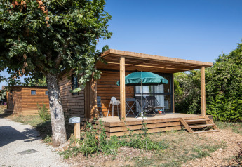Træhytte Chalet Evasion med terrasse, havebord og parasol, omgivet af grønt og blå himmel.