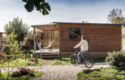 Hombre en bicicleta y mujer en la terraza del Chalet Evasion en Huttopia Meursault, Francia, al sol.