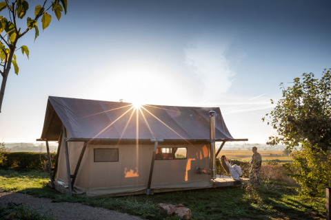 Tienda safari Trapper II en Huttopia Meursault, Francia, iluminada al amanecer con dos personas afuera.