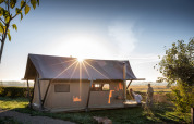 Trapper II safari tent at Huttopia Meursault in France, glowing in the sunrise with two people outside.