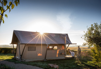 Trapper II safari tent at Huttopia Meursault in France, glowing in the sunrise with two people outside.