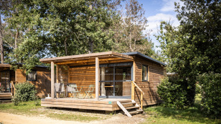 Træhytte Chalet Evasion omkranset af træer med terrasse og havemøbler i solskin.