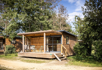 Træhytte Chalet Evasion omkranset af træer med terrasse og havemøbler i solskin.