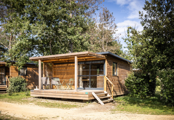 Chalet Evasion houten blokhut met veranda en stoelen, omgeven door bomen in een rustige omgeving.