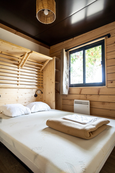 Dormitorio en Chalet Evasion con paredes de madera, cama doble y ventana en Huttopia Vallée de la Semois, Bélgica.