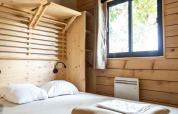 Dormitorio en Chalet Evasion con paredes de madera, cama doble y ventana en Huttopia Vallée de la Semois, Bélgica.