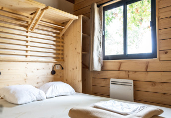 Soveværelse i Chalet Evasion med trævægge, dobbeltseng og vindue, Huttopia Vallée de la Semois, Belgien.