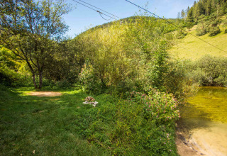 Vista pintoresca de un campo verde junto a un arroyo en un parque vacacional con glamping disponible.