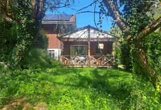 Glampinghut in een vakantiepark, met houten terras, omringd door bomen en een zonnig grasveld.