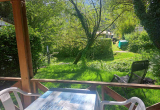 Vista desde el porche de un glamping hacia un jardín verde y árboles en un parque de vacaciones.