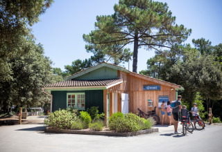 Bezoekers staan bij het onthaal van Huttopia Oléron Les Chênes Verts, een vakantiepark tussen bomen.