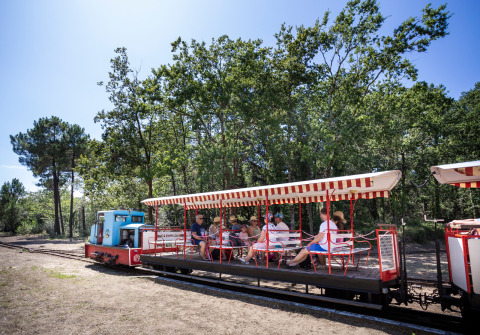 Familias viajando en un pequeño tren abierto en Huttopia Oléron Les Chênes Verts, parque vacacional en Francia.