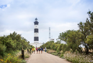 Een groep mensen wandelt langs een pad vol bloemen en bomen naar een vuurtoren in Frankrijk.
