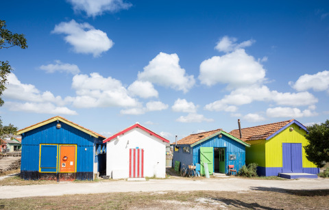 Bunte Strandhütten unter blauem Himmel mit Wolken im Huttopia Oléron Les Chênes Verts, Nouvelle-Aquitaine, Frankreich.