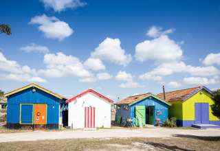 Bunte Strandhütten unter blauem Himmel mit Wolken im Huttopia Oléron Les Chênes Verts, Nouvelle-Aquitaine, Frankreich.