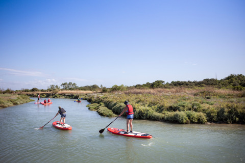 Personas practicando paddle surf en un río estrecho rodeado de vegetación en Huttopia Oléron Les Chênes Verts, Francia.
