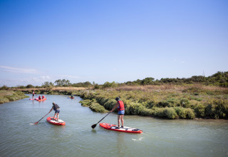 Menschen beim Stand-Up-Paddling auf einem ruhigen Fluss im Ferienpark Huttopia Oléron Les Chênes Verts, Frankreich.