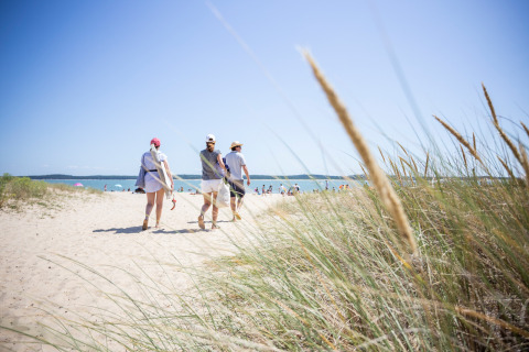 Three people walk through sandy dunes towards the beach at Huttopia Oléron Les Chênes Verts holiday park, France.
