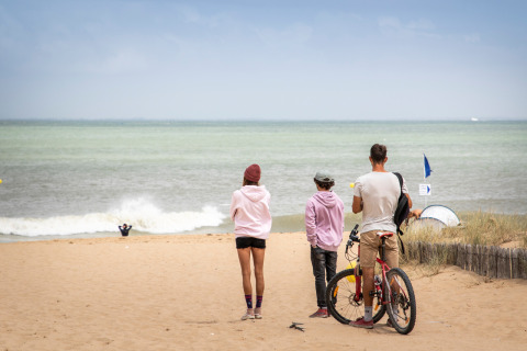 Tres personas y una bicicleta en la arena de una playa cerca de Dolus d'Oléron, Francia, mirando el mar.