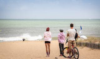 Drei Personen und ein Fahrrad am Strand bei Dolus d'Oléron, Frankreich, blicken auf das Meer.