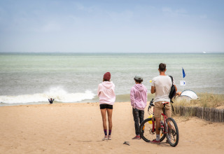 Drie personen en een fiets op het strand bij Dolus d'Oléron in Frankrijk, met zicht op de zee.