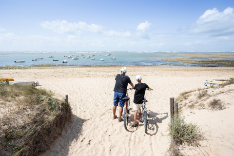 Deux personnes avec des vélos regardent la plage et la mer près de Dolus d'Oléron, Nouvelle-Aquitaine, France.