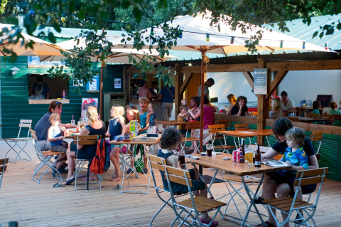 Familias cenan al aire libre bajo sombrillas en Huttopia Oléron Les Chênes Verts, un parque vacacional en Nouvelle-Aquitaine.