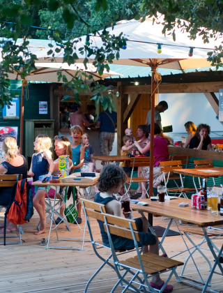 Familias cenan al aire libre bajo sombrillas en Huttopia Oléron Les Chênes Verts, un parque vacacional en Nouvelle-Aquitaine.