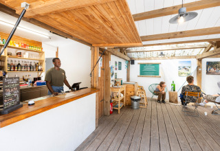 Receptie in vakantiepark Huttopia Oléron Les Chênes Verts met medewerker en relaxte gasten in de lounge.