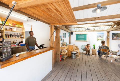 Receptie in vakantiepark Huttopia Oléron Les Chênes Verts met medewerker en relaxte gasten in de lounge.