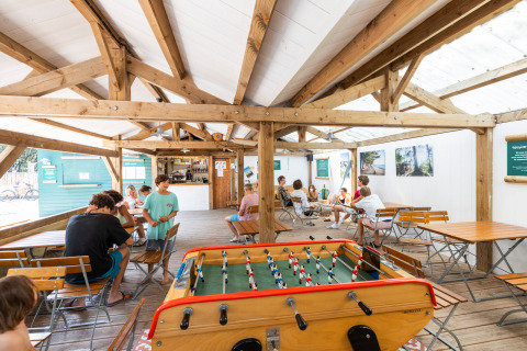 Indendørs fællesområde på Huttopia Oléron Les Chênes Verts med bordfodbold og siddepladser.