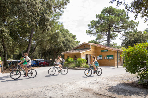 Des vacanciers font du vélo devant un bâtiment en bois à Huttopia Oléron Les Chênes Verts, France.