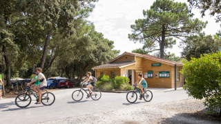 Gäste fahren Fahrrad vor einem Holzgebäude im Ferienpark Huttopia Oléron Les Chênes Verts in Frankreich.