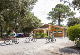 Huéspedes pasean en bicicleta frente a un edificio de madera en Huttopia Oléron Les Chênes Verts, Francia.
