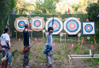 Three people practice archery at an outdoor range with targets at Huttopia Oléron Les Chênes Verts in France.