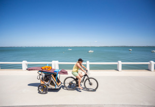 Donna in bicicletta con rimorchio pieno di attrezzatura da spiaggia sul mare a Huttopia Oléron Les Chênes Verts.