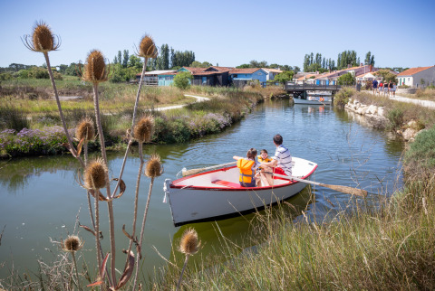 Una familia navega en bote por un canal cerca de Dolus d’Oléron, rodeados de naturaleza y casas.