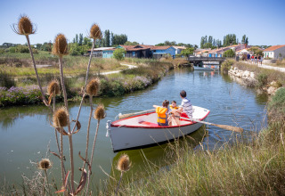 Une famille rame sur un canal près de Dolus d’Oléron parmi la nature et les maisons du village.