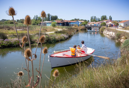 Familie rudert in einem kleinen Boot durch einen Kanal bei Dolus d’Oléron, von Natur umgeben.