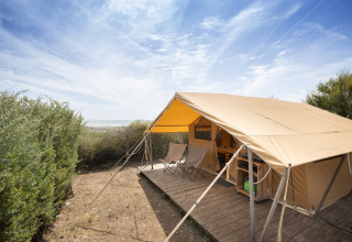 Tienda safari Bungalow Classic en Huttopia Côte Sauvage, Francia, con terraza de madera y sillas.