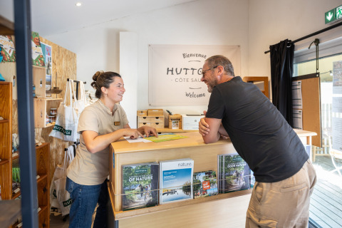 Recepcionista conversa con un huésped en el mostrador de Huttopia Côte Sauvage, Nouvelle-Aquitaine, Francia.