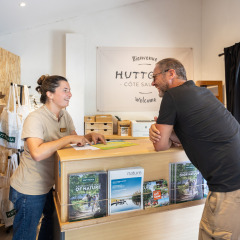 Receptionist talking with a guest at the front desk of Huttopia Côte Sauvage holiday park, Nouvelle-Aquitaine, France.
