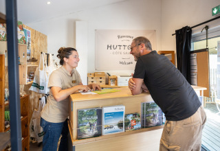 Receptionist parla con un ospite al banco di Huttopia Côte Sauvage, Nouvelle-Aquitaine, Francia.